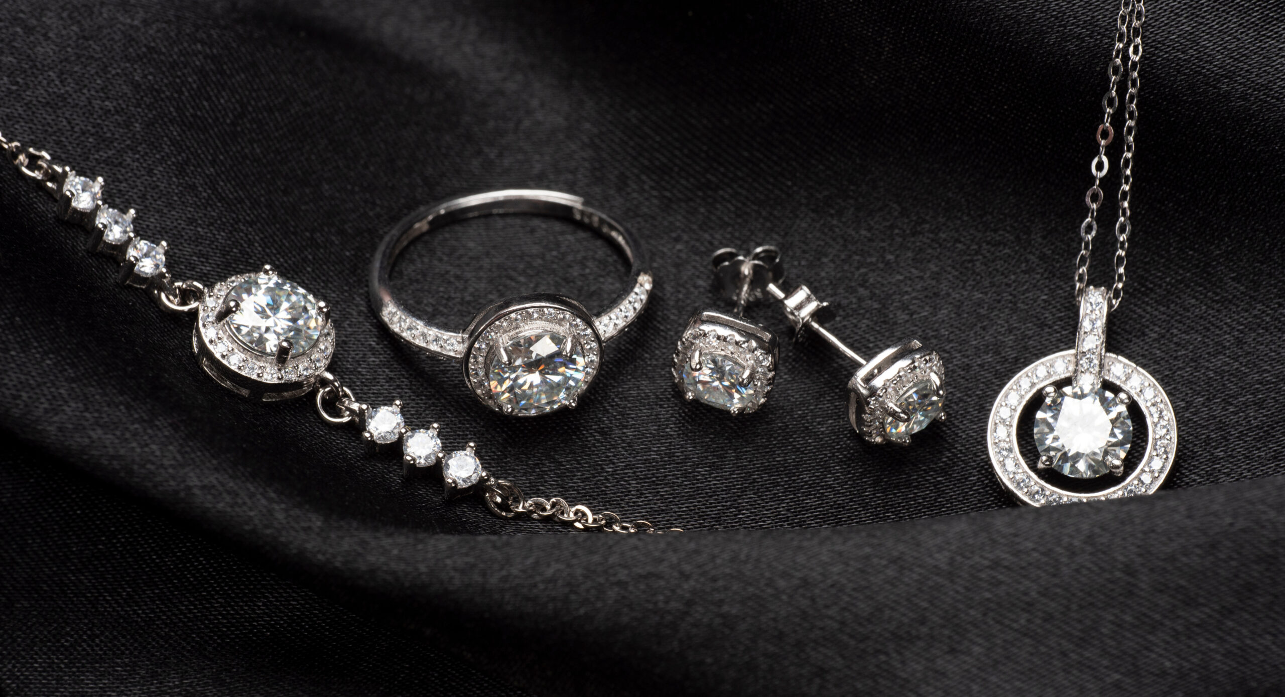 Diamond engagement ring, bracelet, and stud earrings on black fabric